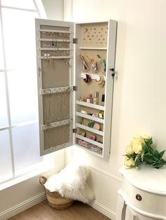 an open cabinet with jewelry in it next to a white table and flower vases