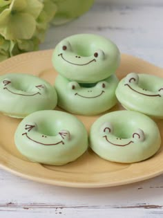 four green donuts with faces drawn on them sitting on a plate next to flowers