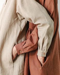 a woman wearing a brown shirt and tan pants with her hands on the back of her jacket