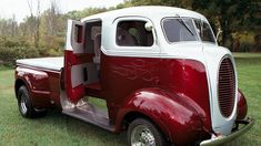 an old red and white truck parked in the grass