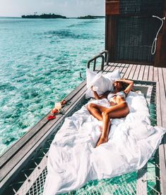 a woman laying on top of a white bed next to the ocean in front of a wooden pier