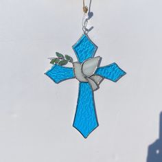 a stained glass cross hanging from a chain on a white wall with a shadow cast in the background