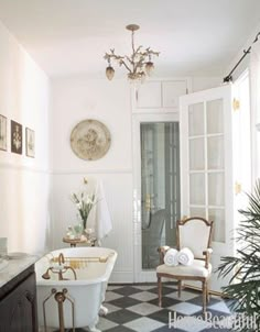 a bathroom with black and white checkered flooring, chandelier above the bathtub