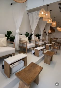 a room filled with white couches and wooden tables next to hanging light fixtures on the ceiling