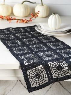 the table runner is decorated with black crocheted doily and white pumpkins