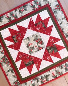 a red and white quilted table topper on a wooden floor with holly decorations