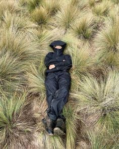 a man is laying in the grass wearing a black jacket and hat with his eyes closed