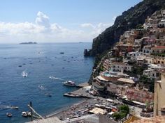 boats are floating in the water near a city by the ocean and cliffs with houses on them