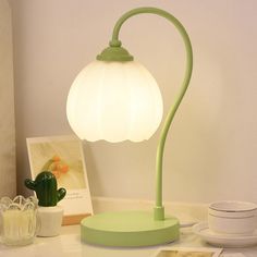 a green table lamp sitting on top of a white counter next to a cactus plant