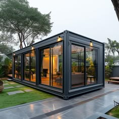 a house made out of shipping containers sitting on top of a lush green field next to a tree