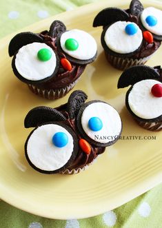 four cupcakes decorated with white frosting and colorful candy eyes on a yellow plate