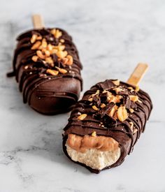 two pieces of chocolate covered ice cream with nuts on top, sitting on a marble surface