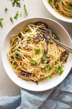 two bowls of pasta with mushrooms and parsley on the side, one has a fork in it