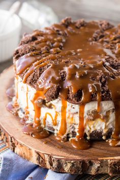 a cake covered in ice cream and caramel drizzle on a wooden platter