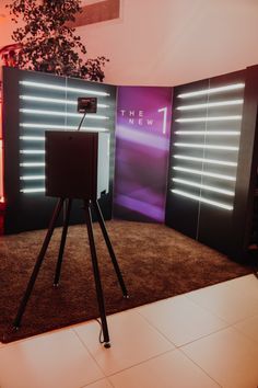 a speaker on a tripod stands in front of a television screen with the new 1 logo