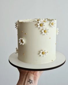 a hand holding a white cake with daisies on it