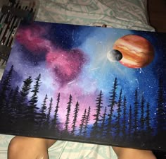 a person holding up a painting with trees and planets in the sky above them on a bed