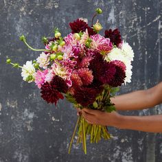 a woman holding a bouquet of flowers in her hands with an old wall behind her