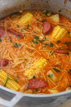 a pot full of soup with corn on the cob and pepperoni in it