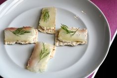 four pieces of food on a white plate with some green garnish around it