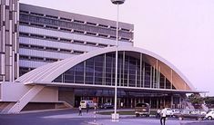 a large building with cars parked in front of it and people walking around the outside