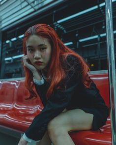 a young woman with red hair sitting on a bench in front of a train car