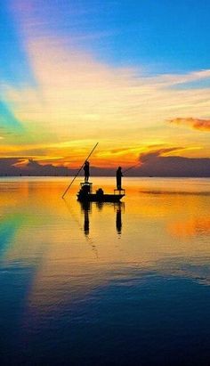 two people standing on a boat in the middle of water at sunset with colorful clouds