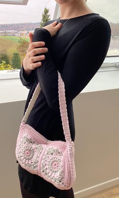 a woman is holding a pink crocheted purse in front of her face and looking out the window