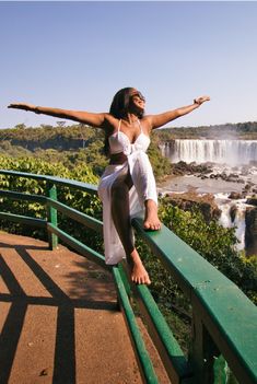 a woman standing on top of a green rail next to a waterfall