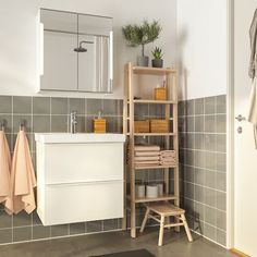 a bathroom with grey tile walls and white fixtures, including a wooden shelf for towels