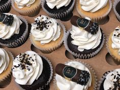 cupcakes with white frosting and black sprinkles are arranged in a box