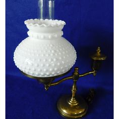 a white glass vase sitting on top of a brass stand next to a blue wall