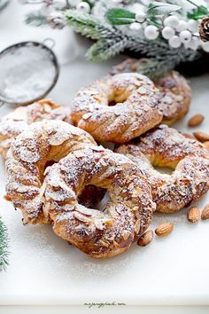 almonds and powdered sugar covered donuts on a white surface next to pine branches