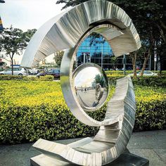 a metal sculpture sitting on top of a sidewalk next to a lush green park filled with trees