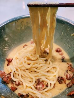 the noodles are being held by chopsticks in a bowl with bacon and cream sauce