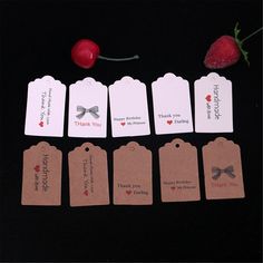 small tags with bows and hearts are arranged on a black surface next to a strawberry