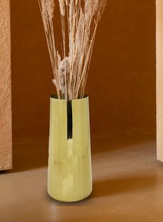 a vase filled with dry grass sitting on top of a table next to a wall