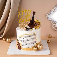 a white and gold birthday cake with musical notes on the front, guitar decoration atop it