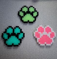 three pieces of perler bead art on a gray surface, one is pink and the other is green