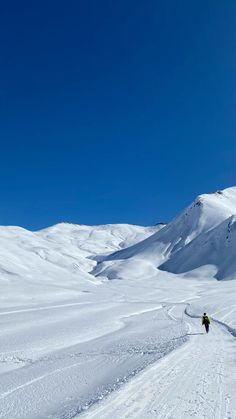 two people skiing down a snow covered slope on a sunny day with mountains in the background