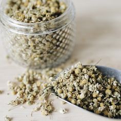 a spoon full of dried herbs next to a jar filled with it's contents