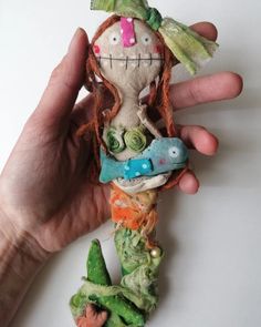 a hand holding a small doll in the shape of a mermaid with long red hair