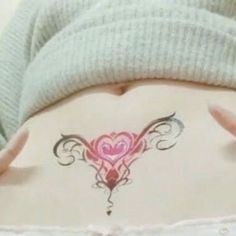 a woman's stomach with a heart tattoo on the side and her hands behind her back