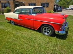 an old red and white car is parked in the grass near a brick building on a sunny day