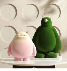 two green and pink stuffed animals sitting on top of a white table next to each other