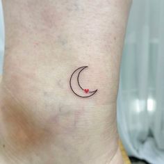 a small tattoo on the ankle of a woman's lower leg with a crescent moon and red heart