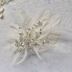 a brooch with feathers and crystal stones on white furnishing next to flowers