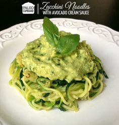 a white plate topped with pasta covered in pesto sauce and green leafy garnish