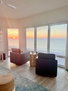 a living room filled with furniture and large windows overlooking the ocean at sunset or sunrise