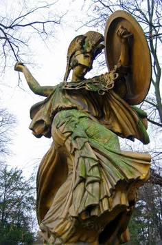 a statue of a woman holding a shield in her hand and standing next to trees